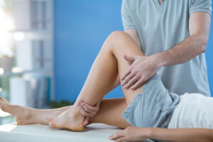 A male massage therapist works on the knee of a patient or client wearing shorts and a shirt.